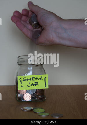 Un vetro giurare jar con un'etichetta gialla su un tavolo di legno con una mano mettere il denaro nel vaso Foto Stock