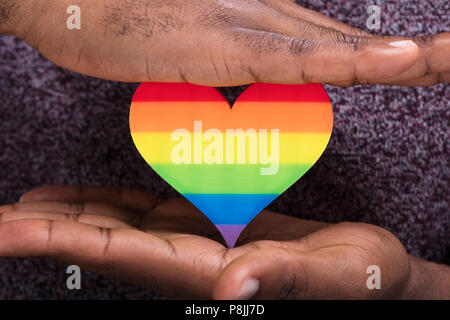 Close-up di una mano di un uomo proteggere striscia colorata cuore oltre la scrivania bianca Foto Stock