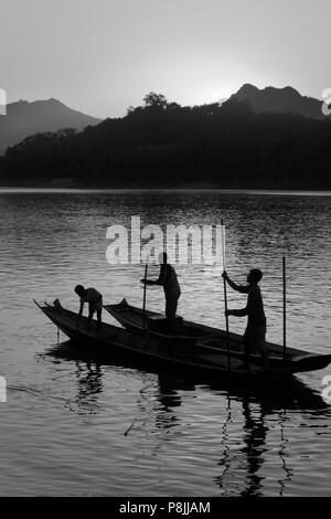 Il sole tramonta su una collina sul fiume Mekong scontornamento laotiani il polling della loro barca fluviale che corre attraverso - Luang Probang, LAOS Foto Stock