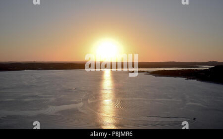 Il sole tramonta in un brillante tripudio di giallo e arancione sopra il Lago Travis di Austin, TX Foto Stock