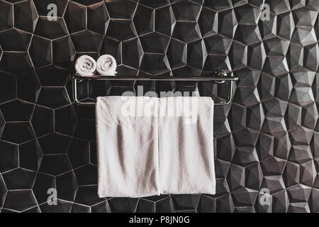 Pulire quattro asciugamani bianchi sul supporto in hotel bagno con trama parete nera. Stile moderno e minimale Foto Stock