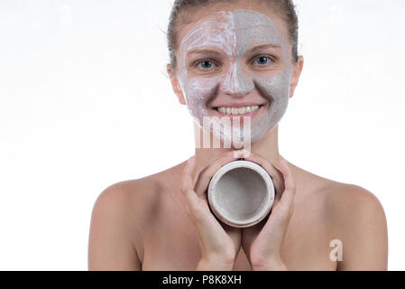 Due maschera di cosmetici di argilla grigia con scrub e crema sulla faccia di una giovane e bella ragazza e un vaso con argilla Foto Stock