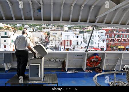 Capri, Italia - 18 Maggio 2013: il capitano della nave si trova presso il banco di comando e il paesaggio dell'isola in background Foto Stock