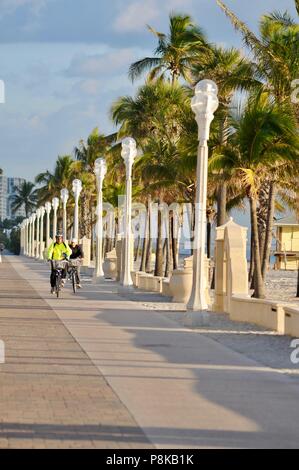 Persone in bicicletta lungo la popolare palm alberata, lastricata Hollywood Beach Boardwalk, con attraenti lampioni, in Hollywood, Florida, Stati Uniti d'America. Foto Stock