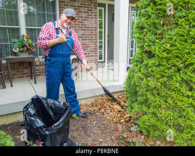 Felice giardiniere o lavoratore fino a rastrellare foglie nella parte anteriore di una casa residenziale pausa di sorridere alla telecamera Foto Stock