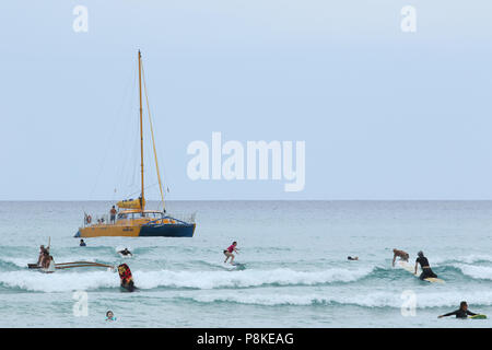 Imbarcazione a vela denominata Manu Kai per turisti. Surfers e persone in acqua sono visibili. La spiaggia di Waikiki, Waikiki, Honolulu Oahu Island, Hawaii, Stati Uniti d'America. Foto Stock