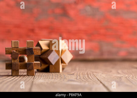 Due puzzle in legno i cubi su una tavola di legno in un angolo basso fuoco selettivo vista con spazio copia contro una messa a fuoco morbida dello sfondo rosso Foto Stock