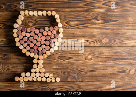 Il design creativo di una piena wineglass realizzata con tappi di sughero da vino rosso e bianco di bottiglie su di un legno rustico sfondo con spazio di copia Foto Stock