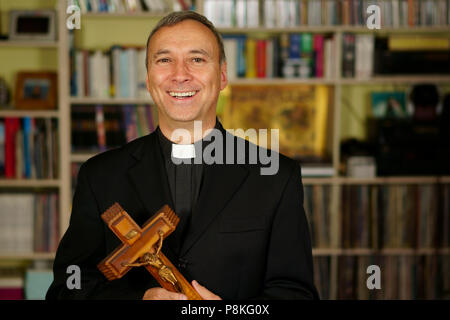 Una buona ricerca di sorridere e ridere sacerdote cattolico è che mostra un crocifisso. Egli ci guardano con interesse, pensiveness, proselitismo, gioia e felicità Foto Stock