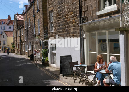 Due persone che sedeva al tavolo esterno cafe in strada a Robin Hood's Bay,Yorkshire Costa Patrimonio,l'Inghilterra,UK Foto Stock