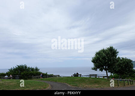 Due persone sat su banco affacciato sul mare sulla rupe a Robin Hood's Bay,Yorkshire,l'Inghilterra,UK con grande sky,mare e gli alberi in corrispondenza di ciascun lato. Foto Stock