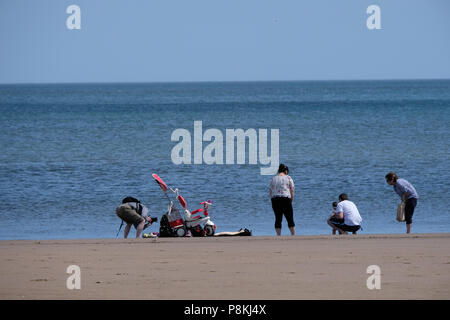 I vacanzieri seduti da, guardando le onde e passando per una racchetta in mare nel North Yorkshire holiday resort di Scarborough,UK sulla baia del nord Foto Stock