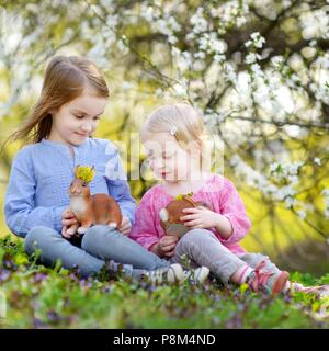 Due adorabili poco sorelle giocando con conigli pasquali in fioritura spring garden il giorno di Pasqua Foto Stock