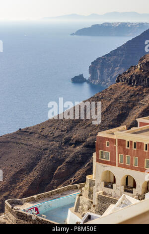 Scena vulcanica di Santorini. La fine di Oia, Grecia. Incredibile vista diurna verso il profondo mare acque cristalline con casa abbandonata e marrone e nero Foto Stock