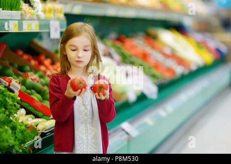 Bambina scegliendo i pomodori in un negozio di alimentari Foto Stock