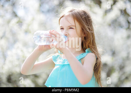 Adorabile bambina acqua potabile in ciliegio in fiore giardino sul sole e caldo giorno d'estate Foto Stock