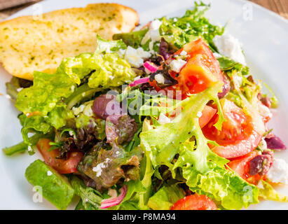 Close up soleggiato insalata estiva sulla piastra bianca con lattuga, pomodori, il formaggio feta, cipolla rossa, avocado Foto Stock