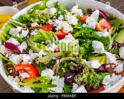 Close up soleggiato insalata estiva in bianco ciotola sul patio esterno tavolo, con lattuga, pomodori, il formaggio feta, cipolla rossa, avocado Foto Stock