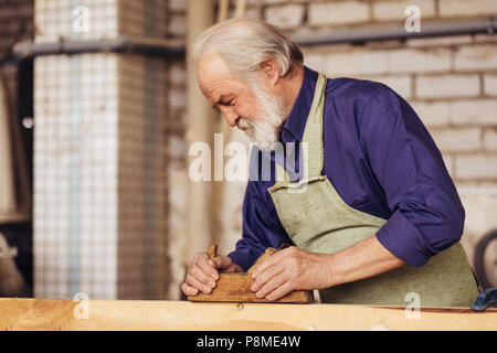 Close-up vista laterale immagine di senior citizen la levigatura di legno per mobili Foto Stock