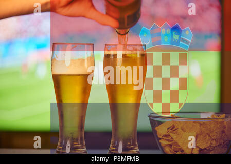 Doppia esposizione della bandiera croata e due bicchieri di birra nella parte anteriore della TV a giocare il gioco del calcio Foto Stock