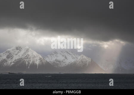 Sole su montagne coperte di neve sotto un cielo scuro Foto Stock