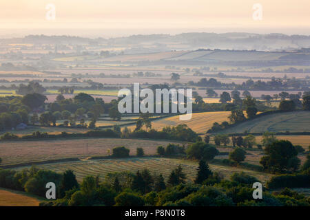 Vista su dei terreni agricoli del Warwickshire in misty luce del sole di mattina preso da Downs sopra il villaggio di Ilmington, il Costwolds, Warwickshire, Inghilterra Foto Stock