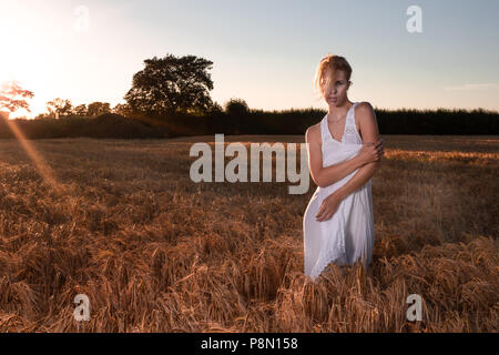 Tramonto con femmina bionda in piedi in un campo Foto Stock
