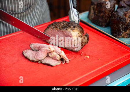 Lo Chef mani tutto il taglio di agnello alla griglia per le bistecche con il coltello sul tagliere. Hot piatti a base di carne Foto Stock