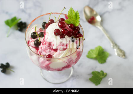 Cremoso gelato con ribes rosso e nero in un bicchiere su un tavolo luminoso. Messa a fuoco selettiva. Foto Stock