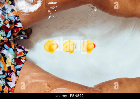 Elevato angolo di visione di un giovane uomo caucasico che indossa un costume da bagno rilassante, circondato da gomma anatre, nella vasca del bagno Foto Stock