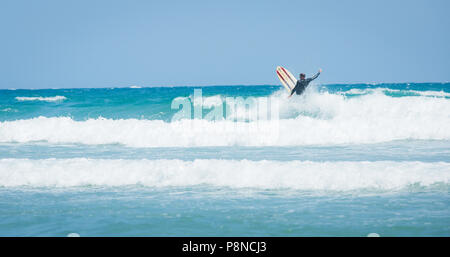 Un surfista al largo della costa della Cornovaglia cavalcare le onde bianco sulla sua tavola da surf prima di un wipeout. Foto Stock