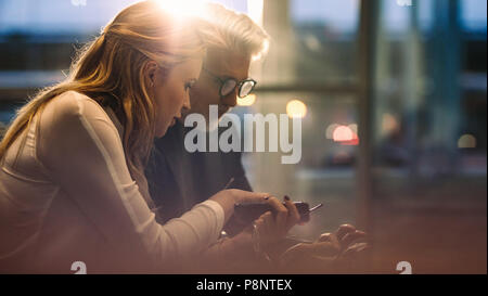 Business colleghi seduti insieme nella lobby di Office e utilizzare i loro telefoni cellulari. I professionisti aziendali utilizzando i telefoni cellulari durante una pausa in ufficio. Foto Stock