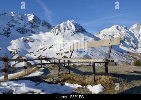 Banco solitario di fronte coperta di neve i prati alpini alla fine dell'inverno al Col de Lautaret Foto Stock