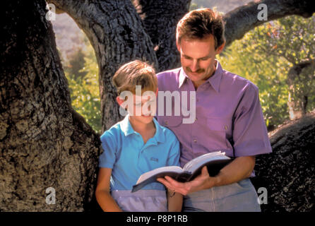 Padre leggendo la Bibbia con figlio sotto grandi alberi. Signor © Myrleen Pearson Foto Stock