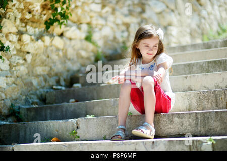 Adorabili poco ragazza seduta sulle scale sul sole e caldo giorno d'estate in tipica città italiana Foto Stock