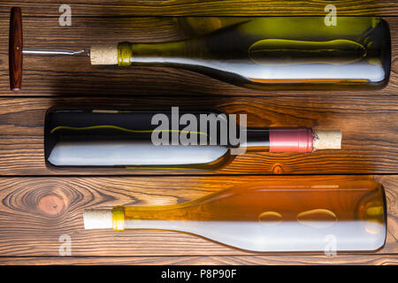 Angolo di alta vista di tre bottiglie di vino che giace contro lo sfondo di legno Foto Stock