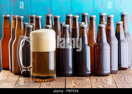 Selezione di più flaconi non marcato di in casa la birra artigianale con un pieno spumoso il boccale in primo piano su un picnic in legno tabella contro una textur Foto Stock