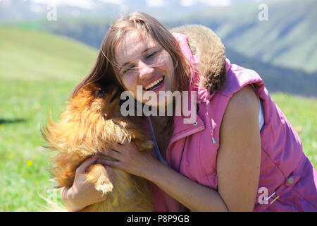 Un piccolo cane rosso (Pomerania Spitz) lambisce un volto di donna forzando la sua a ridere. Foto Stock