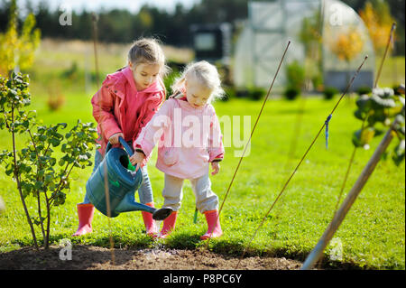 Due adorabili poco mamma aiutanti di impianti di irrigazione nel giardino sulla bellissima giornata autunnale Foto Stock