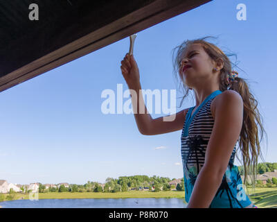 Bambina aiutando con la colorazione del nuovo gazebo in piedi su una scala pittura lo scudo anteriore con un rurale suburbana di sfondo del lago Foto Stock