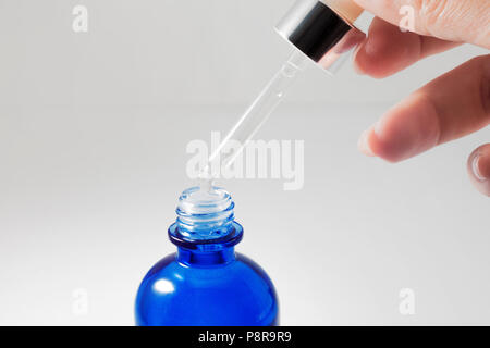 Utilizzare il siero, cosmetici. Mano femmina trattiene la pipetta con siero di cosmetici. Close up Foto Stock