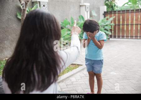 Arrabbiato madre scolding figlia che copre il volto in salotto Foto Stock