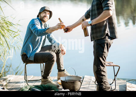 Due pescatori rilassante insieme con la birra mentre la pesca sul lago al mattino Foto Stock