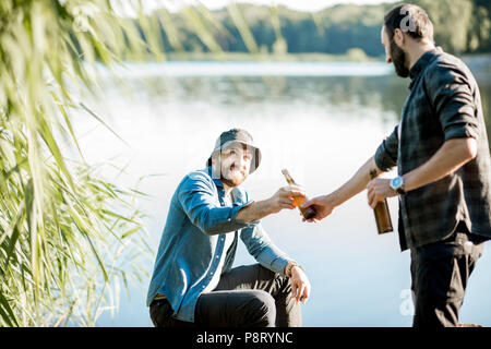 Due pescatori rilassante insieme con la birra mentre la pesca sul lago al mattino Foto Stock