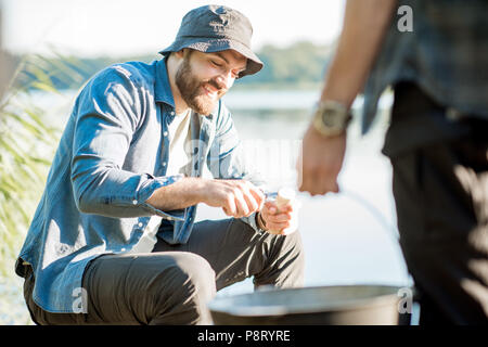 Due pescatori la preparazione di alcuni alimenti durante il picnic sul molo in legno vicino al lago al mattino Foto Stock