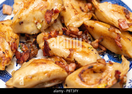 Varenyky, vareniki, pierogi, pyrohy o gnocchi di patate, con ripieno di formaggio e patate servita con cipolla e pancetta affumicata su una piastra di colore blu Foto Stock