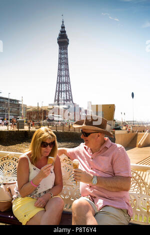 Regno Unito, Inghilterra, Lancashire, Blackpool, North Pier, visitatori sat sul banco di prova nella luce del sole di mangiare gelati Foto Stock