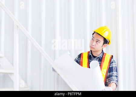 Smart ingegnere civile indossare l'elmetto di sicurezza e tenere la costruzione e architetto progetto blueprint in mano e verificare la progettazione dei lavori in ufficio sito in b Foto Stock