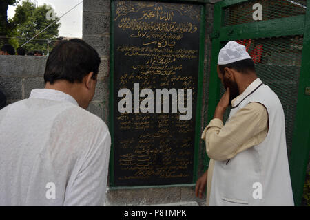 Budgam, Jammu e Kashmir in India. 13 Luglio, 2018. Il Kashmir uomini musulmani leggere il nome dei martiri durante la ghirlanda recante cerimonia al martire il cimitero a Srinagar, la capitale estiva della controllata indiana Kashmir India, durante una cerimonia di premiazione che si terrà a segnare il martirio anniversario della Kashmiris ucciso dall'esercito di un re indù. Le autorità indiane a Srinagar distribuito migliaia di personale di sicurezza nelle principali città di Srinagar per impedire l'anti-Indiani proteste nell'area del centro cittadino di Srinagar. Ogni anno il 13 luglio Kashmir osserva il martirio anniversario di 23 musulmani che erano stati uccisi da t Foto Stock