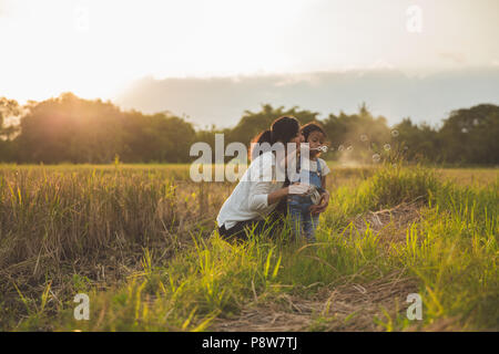 Mamma e Bambino gioca con bolla di risone di campo durante l'estate tramonto Foto Stock